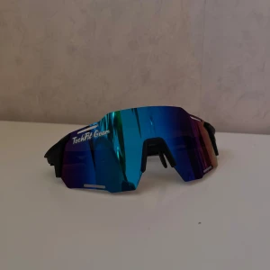 Blå sportglasögon från TechFit Gear - Snygga sportglasögon från TechFit Gear med en spegelblå lins och svart båge. Perfekta för utomhusaktiviteter med en modern och aerodynamisk design. Lätta och bekväma att bära under långa perioder.
