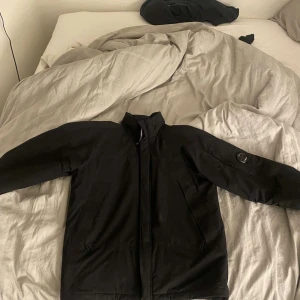 Svart jacka från C.P. Company - Säljer en stilren svart jacka från C.P. Company. Jackan har en dragkedja framtill och en cool detalj på ärmen. Perfekt för våren.