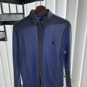 Blå skjorta från Ralph Lauren - Snygg blå långärmad skjorta från Ralph Lauren med klassisk krage och knappar framtill. Skjortan har en broderad logotyp på bröstet och är tillverkad i ett bekvämt material.