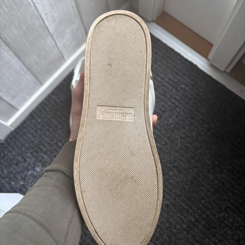 Snygga vita sneakers från Burberry med klassiskt rutigt mönster på hälen. Skorna har snörning och en stilren design med detaljer i mocka och syntetmaterial. Perfekta för en trendig look. Köpte för 6800 Allt Og ingår. Kengät.