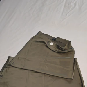 Olivgrön långkjol från Lindex - Snygg olivgrön långkjol från Lindex i ett glansigt material. Kjolen är tillverkad av återvunnen polyester och har en elegant och flytande passform. Perfekt för att ge en stilren touch till din outfit.