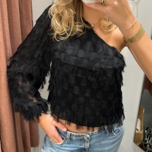 Svart oneshoulder topp - Snygg svart oneshoulder topp med fransiga detaljer och ett unikt rutmönster. Perfekt för en kväll ute eller middag🙌🏻Den fäller lite fransar ibland med det gjorde den redan i butiken!
