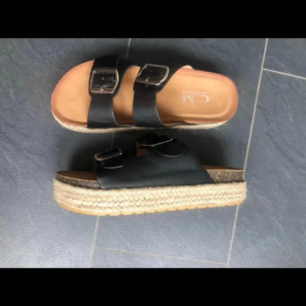 Snygga svarta sandaler från CM med dubbla remmar och justerbara spännen i silver. Sandalerna har en bekväm fotbädd och en flätad sula som ger en stilren look. Perfekta för varma dagar!. Kengät.