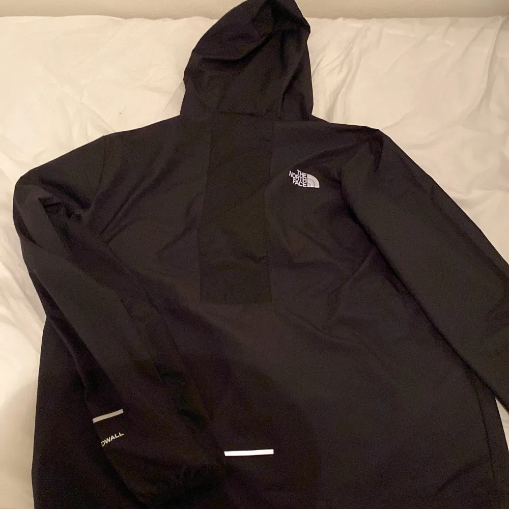 Säljer en svart vindjacka från The North Face. Jackan har en huva och dragkedja framtill. Perfekt för blåsiga dagar och har en stilren design med The North Face-logga på bröstet. Kan gå ner i pris vid snabb affär. Takit.