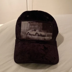 Svart keps med bilmotiv - Cool svart keps med ett tryck av en klassisk bil på framsidan. Kepsen har ett nätmaterial på baksidan för ventilation och en justerbar rem för perfekt passform. Kan gå ner i pris