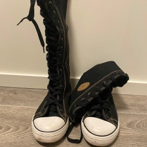 Svarta knähöga sneakers med snörning - Svarta knähöga sneakers med snörning och dragkedja på sidan. De har en vit tå och sula med kontrasterande sömmar. 