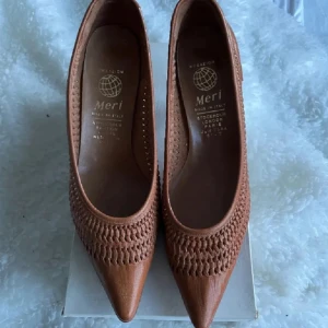 Bruna pumps från Meri - Snygga bruna pumps från Meri med spetsig tå och flätad detalj på ovansidan. Perfekta för en elegant look. Tillverkade i skinn för en lyxig känsla.