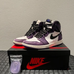 Nike Air Jordans i lila och vit - Snygga Nike Air Jordans i en cool lila och vit färgkombination. Skorna har en klassisk hög design med svart snörning och en ikonisk Nike-logga på sidan. Perfekta för att ge din outfit en sportig touch. Extra lila skosnören medföljer.