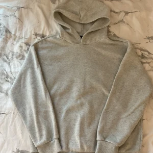 Grå hoodie med disco-tryck - Ljusgrå hoodie med huva och långa ärmar. På ryggen finns ett coolt tryck med två discobollar och texten 'Disco Club'. Mjuk och skön, perfekt för dig som gillar en avslappnad stil med lite extra attityd.