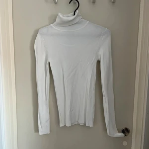 Vit polotröja från Primark XS - Vit, ribbad polotröja från Primark i storlek XS. Tröjan är figurnära med lång ärm och hög polokrage, perfekt att styla med jeans eller kjol. Tillverkad i mjukt, stretchigt material som sitter snyggt på kroppen.