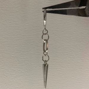 Silvrigt örhänge med kedja och spike - Coolt örhänge i silverfärg med kedjelänkar och en spetsig spike längst ner. Ger en edgy vibe och passar perfekt för dig som gillar statement-smycken. Säljs styckvis.