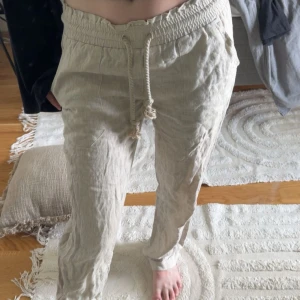 Beiga linnebyxor från Skagen  - Snygga och luftiga beiga linnebyxor från Skagen i 100% linne. Byxorna har elastisk midja med dragsko och avslappnad passform, perfekta för varma dagar. Stilen är enkel och tidlös med raka ben och mjuk känsla. Dom är ej strykta som syns på bilden. Nypris är 921kr