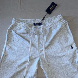 Grå mjukisbyxor från Polo Ralph Lauren, - Snygga ljusgrå mjukisbyxor från Polo Ralph Lauren med klassisk logga broderad på benet. Byxorna har resår i midjan och långa snören för justering. Perfekta för chill dagar eller när du vill vara bekväm men ändå se fräsch ut. Storlek M