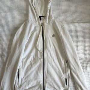 Zip hoodie från Moose Knuckles - Snygg vit ziphoodie från Moose knuckles med dragkedja framtill och två fickor. Den har en del fläckar men som nog går bort med vanish. Fysiskt kvitto finns