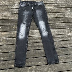 Svarta skinny jeans från Dsquared2 - Säljer ett par svarta  jeans från Dsquared2 med slitningar, blekta partier och coola färgstänk. Jeansen har klassisk femficksdesign, låg midja och smal passform. Materialet är stretchigt denim som sitter snyggt och bekvämt.