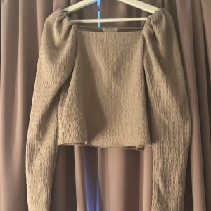 Beige offshoulder topp med struktur - Trendig beige topp med offshoulder och långa ärmar. Toppens tyg är strukturerat och lätt stretchigt, vilket ger en snygg passform. Modellen är croppad och har en stilren, enkel design som passar perfekt till jeans eller kjol!☺️