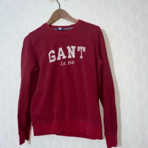 Röd GANT sweatshirt med tryck - Snygg röd sweatshirt från GANT med klassiskt vitt tryck på bröstet och rund hals. Tröjan har långa ärmar och ribbade muddar vid ärmslut och nederkant. Perfekt för dig som gillar en sportig och avslappnad stil.