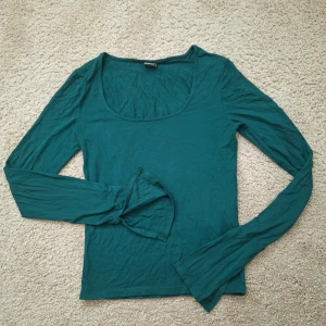Mörkgrön långärmad topp Gina Tricot - En enkel och stilren mörkgrön långärmad topp från Gina Tricot. Modellen har rundad, djup urringning och är tillverkad i mjuk bomullsmix. Perfekt att matcha med jeans eller kjol för en clean look. Endast använd några gånger så I bra skick!