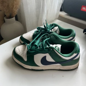 Nike Dunk Low i grönt och vitt - Nike Dunk Low sneakers i vitt och grönt. Är använda ett par gånger men i bra skick.