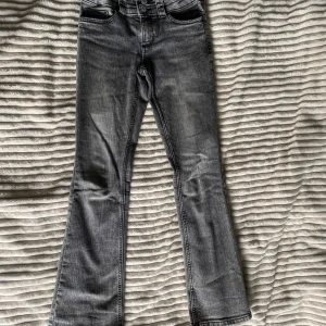 Grå bootcut jeans från H&M - Snygga grå jeans från H&M med bootcut-ben och låg midja. Jeansen har justerbar midja och klassiska fickor både fram och bak. Materialet är en mix av bomull, polyester och elastan för en bekväm passform. Kommer från hem med katt. Hör gärna av dig om du har fler frågor.
