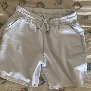 Vita shorts med snörning - Snygga vita shorts med elastisk midja och snörning framtill. De har en avslappnad passform och är tillverkade i mjukt bomullsmaterial. Perfekta för varma sommardagar och chill häng. Två sidofickor för mobilen eller nycklarna.