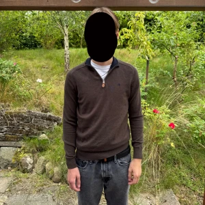 Brun merinoullströja från Morris - Snygg brun långärmad tröja från Morris i 100% merinoull. Tröjan har half zip-dragkedja vid halsen och ribbade muddar. Perfekt för dig som gillar klassisk stil med en modern touch. Har en lagning på ryggen syns på bilden 