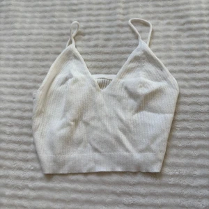 Vit ribbad linnetopp med smala band - Superfin vit ribbad linnetopp med smala axelband och v-ringning. Toppen är croppad och har en mjuk, stretchig känsla som passar perfekt till jeans eller kjol. Enkel och stilren design som är lätt att matcha.