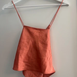 Korallfärgad linnetopp från Monki - Superfin orange topp i satinliknande material från Monki. Faller fint och blir superfin bak i ryggen med ”korsande” band (se sista bilder). Storlek XXS. Mycket bra skick. 