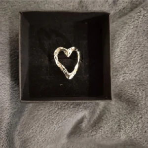 Silvrig hjärtformad ring - Unik ring i silverfärg med ett öppet hjärta som har en lite ojämn, handgjord känsla. Perfekt accessoar för dig som gillar stilrena men ändå personliga smycken. Kommer i en snygg svart ask.