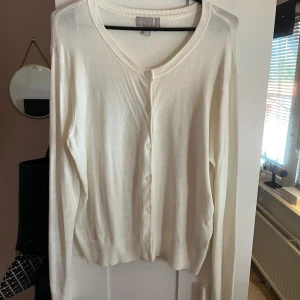 Vit stickad kofta från H&M - Klassisk vit kofta från H&M i storlek L. Den har rund halsringning, långa ärmar och knäppning framtill med matchande knappar. Materialet är tunt och mjukt, perfekt för lager-på-lager. Ribbstickade muddar vid ärmslut och nederkant ger en clean look. Tröjan är endast använd 2-3 gånger och är i ett mycket bra skick! 