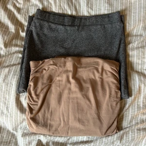 Två tighta kjolar i grått och beige - Säljer två tighta kjolar, en i mörkgrå och en i beige. Båda är korta och har enkel, stilren design utan mönster. Perfekta att matcha med en stickad tröja eller t-shirt. Materialet känns mjukt och stretchigt för en bekväm passform. 