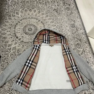 Grå Burberry hoodie med rutigt foder - Snygg grå hoodie från Burberry med dragkedja och klassiskt rutigt foder i huva och insida. Tröjan har snörning i huvan, långa ärmar och är tillverkad i mjuk bomull. Perfekt för dig som vill ha en stilren och lyxig look med en touch av ikoniskt mönster.