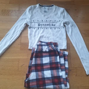 Vit långärmad tröja Dreamlike H&M - Helt ny oanvänf pyjamas som bara har tvättats.Vit långärmad tröja från H&M med svart texten 'Dreamlike' och hjärtmönster över bröstet. Tröjan har v-ringning med spetskant och liten rosett. Materialet är ribbad bomull med lite stretch, perfekt för mysiga dagar.