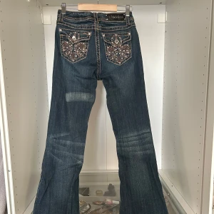 Mörkblå LÅNGA bootcut jeans med pärldetaljer - Snygga LÅNGA mörkblå bootcut jeans från LA Idol USA med coola pärl- och paljettbroderier på bakfickorna. Jeansen har kontrastsömmar och låg midja. Passar dig som är 172+ lång