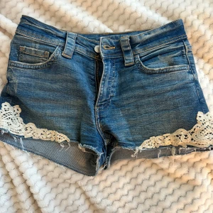 Jeansshorts med spets från H&M - Blå jeansshorts från H&M med råa kanter och snygga vita spetsdetaljer längs bensluten. Super sköna och snygga tyvärr blivit för små💞 