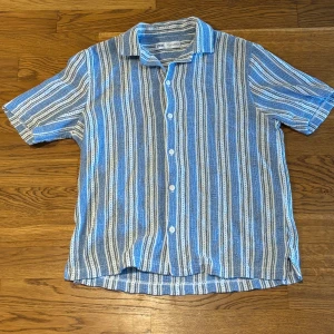 Randig blå skjorta från Zara - Säljer en kortärmad skjorta från Zara i storlek S. Skick 9/10. Använd fåtal gånger och inga skavanker finns. Skjortan har ett randigt mönster i blått, vitt och grått, med klassisk krage och knappar framtill. perfekt för varma sommar och höst dagar. 