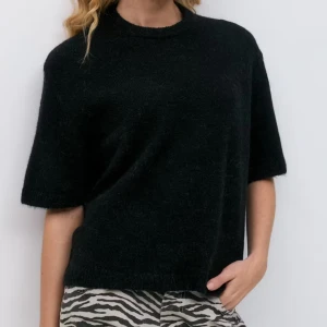 Svart stickad tröja med kort ärm - En svart stickad tröja med rund hals och korta ärmar. Tröjan har en enkel och clean look, perfekt att styla med både jeans och kjol. Mjuk och skön känsla tack vare det stickade materialet.