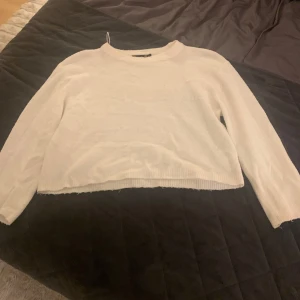 Vit stickad tröja från 157 - Enkel och stilren vit stickad tröja från 157 med rund halsringning och långa ärmar. Tröjan har en rak passform och ribbade muddar vid ärmslut och nederkant. Perfekt att slänga på sig när det är lite kyligare ute.