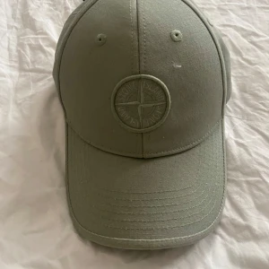 Grön keps från Stone Island Junior - Snygg grön keps från Stone Island Junior med broderad logotyp framtill. Klassisk böjd skärm och justerbar rem baktill. Tillverkad i bomull för en bekväm och stilren look. Perfekt accessoar för att lyfta din outfit.