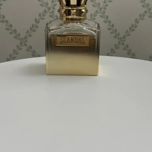 Scandal parfymflaska guld - Lyxig parfymflaska från Scandal i fyrkantig form med snygg guldig gradient och detaljerad kork. Flaskan har en exklusiv känsla med metallisk finish och tydlig logotyp framtill. Perfekt för dig som gillar statement-parfymer och snygg design på sminkbordet. 90 ml kvar av 100ml