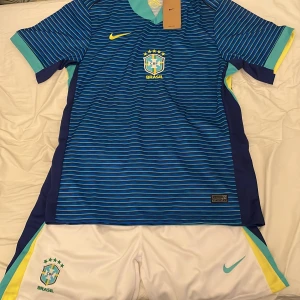 Blå Brasilien fotbollströja Nike - Snygg blå Brasilien fotbollströja från Nike med tunna horisontella ränder i ljusblått och vita detaljer. Tröjan har korta ärmar med turkosa och gula inslag samt Brasilien-emblem på bröstet. Perfekt för dig som älskar fotboll och vill sticka ut på planen. Tröjan är i storlek L men på tröjan står det storlek XXL, vet inte varför men den köptes i Nike. Aldrig använd. 
