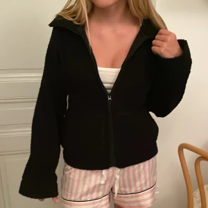 Svart teddyjacka med dragkedja - Mysig svart teddyjacka med hel dragkedja framtill och hög krage. Jackan har lång ärm och en loose passform som ger en chill vibe. Perfekt för lager-på-lager och att slänga på sig när det är kyligt ute. Jätte populär o Stockholmstil💕högt nypris