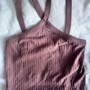 Ribbad brun linnetopp med korsade band - Säljer en ribbad brun linnetopp med smala axelband som korsas i ryggen. Toppen har en tight passform och är tillverkad i mjukt bomullsmaterial. Perfekt för dig som gillar en enkel men snygg look med lite edge.