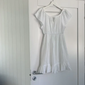 Vit sommarklänning från Lise Sandahl - Superfin vit kortklänning från Lise Sandahl med volangkant nertill och resår i midjan. Klänningen har korta ärmar och en luftig, flowy passform som är perfekt för varma dagar. Tillverkad i mjuk bomull och har en enkel, fräsch look.