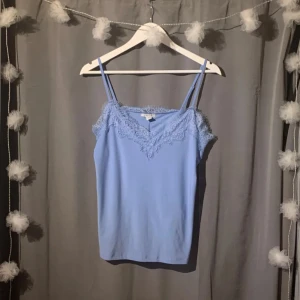 Blå linnetopp - Supersöt ljusblå linnetopp från Amisu med tunna axelband och v-ringning dekorerad med spets. Säljer då den aldrig kommit till användning🩵