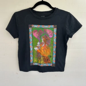 Svart Pink Floyd t-shirt med tryck - Cool svart t-shirt från Urban Outfitters med färgstarkt psykedeliskt tryck framtill. Modellen är croppad och har klassisk rund hals och korta ärmar. Gjord i mjuk bomull, perfekt för dig som gillar bandtröjor och retrostil.