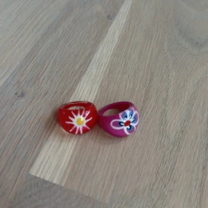 Två färgglada ringar med blommor - Två chunky ringar i plast, en röd med vit och gul blomma och en rosa med blå, vit och röd blomma. Perfekta för att ge din outfit en lekfull och färgstark touch. Båda för 29 kr❤️