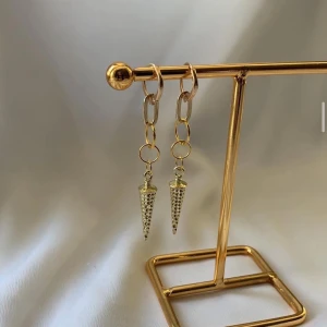 Guldiga örhängen med kedjor och koner - Snygga örhängen i guld med kedjelänkar och spetsiga konformade hängen med små nitar. Ger en edgy vibe och passar perfekt om du vill sticka ut. Lätta att bära och riktigt trendiga.