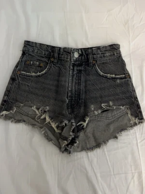 Gråa Zara jeansshorts - Säljer ett par gråa  jeansshorts med råa, fransiga kanter och klassisk femficksdesign. Shortsen kan användas både som högmidjade men även lågmidjade. Använd fåtal gånger.
