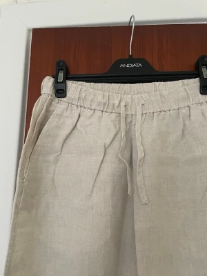Beiga linnebyxor med dragsko - Snygga och luftiga linnebyxor från ARKET. Storlek xs. Beige med raka ben och elastisk midja med dragsko. Byxorna har sidofickor och är perfekta för en avslappnad och trendig stil. Tillverkade i ett lätt och svalt linnematerial.